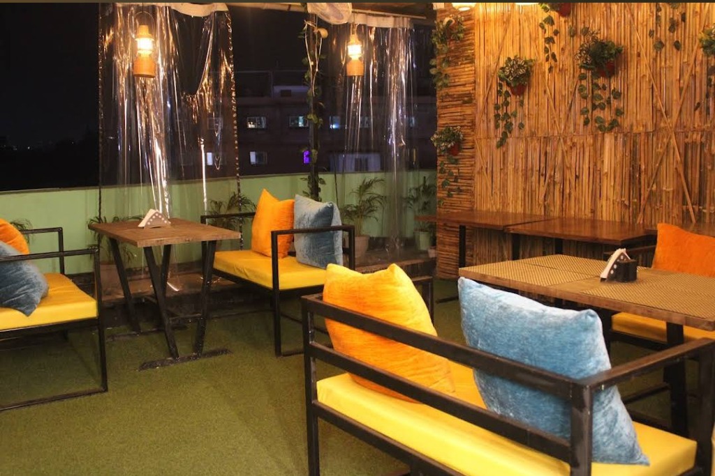 Outdoor rooftop seating with orange and blue cushions and bamboo wall at night
