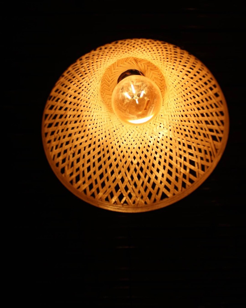 Close-up wicker pendant lamp glowing warm gold on black background